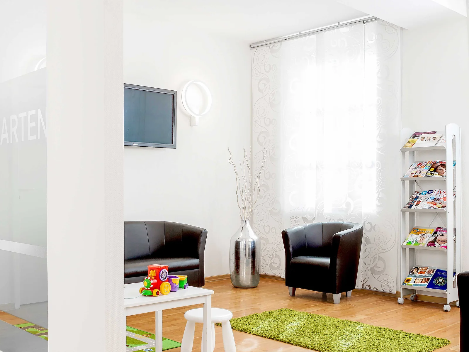Heller Wartebereich der Praxis an der Hochstraße mit Sitzgruppe, Spielecke für Kinder und Zeitschriftenregal